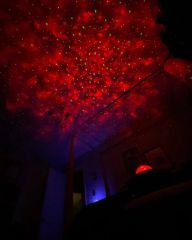 Red nebula and stars projected across a bedroom ceiling